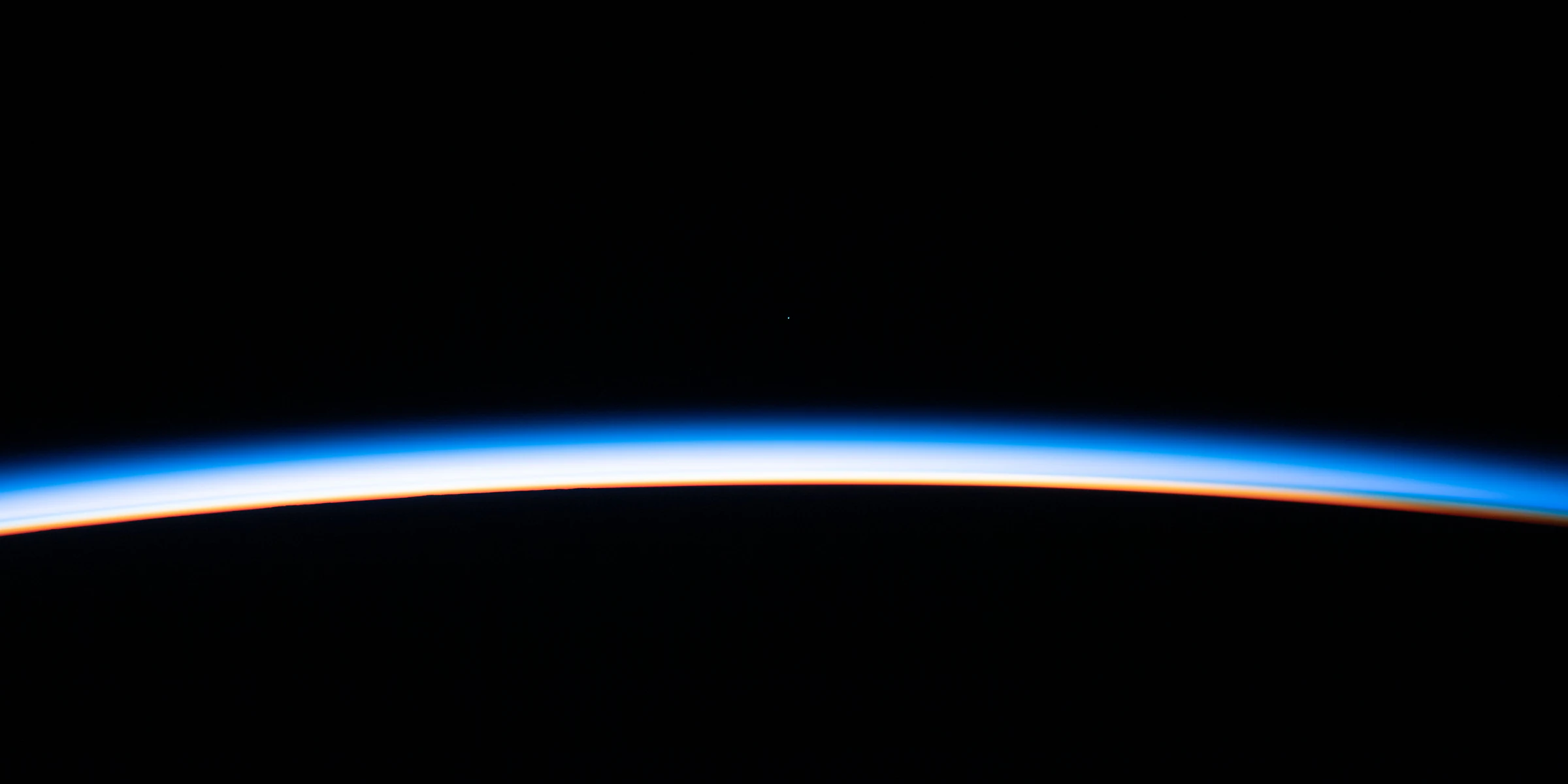 Earth’s horizon from orbit, a thin band of blue and orange light between the dark planet and black space.